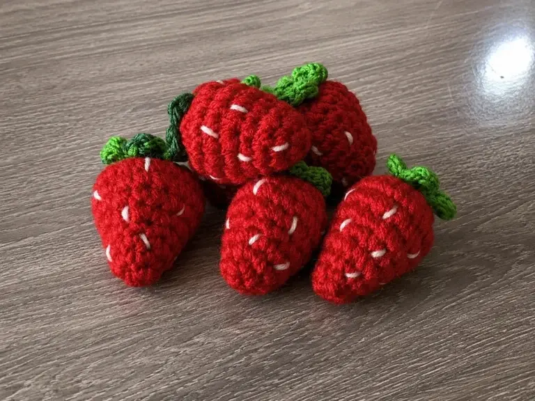Fünf gehäkelte rote Erdbeeren mit grünen Blättern
