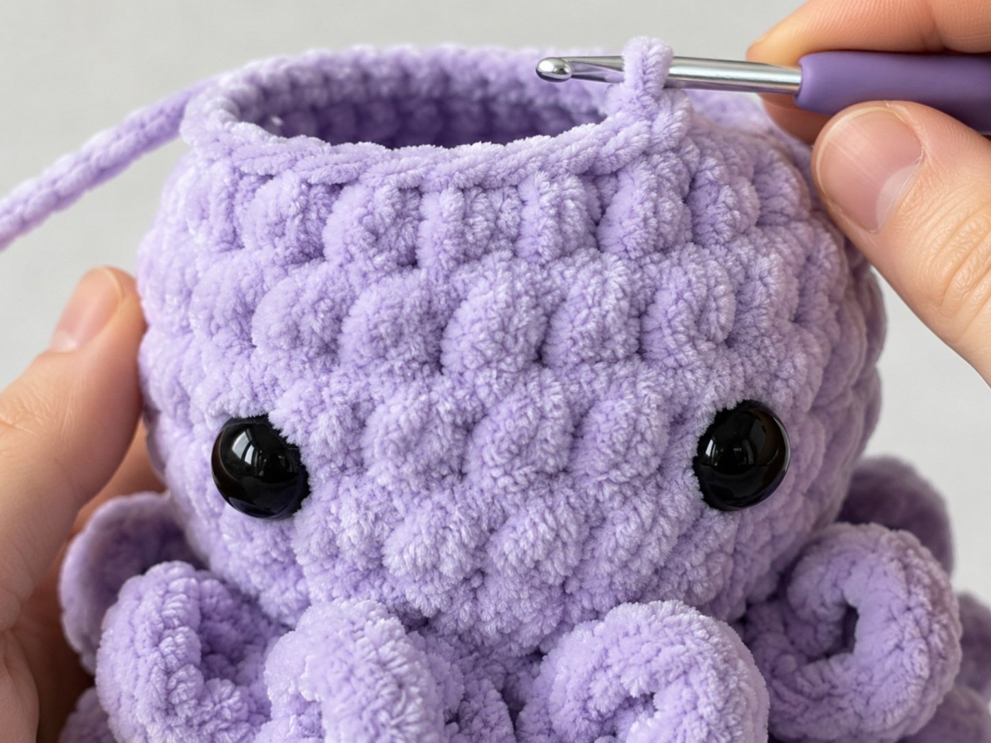 Crochet an octopus step by step: Body with safety eyes inserted and crochet hook in progress.